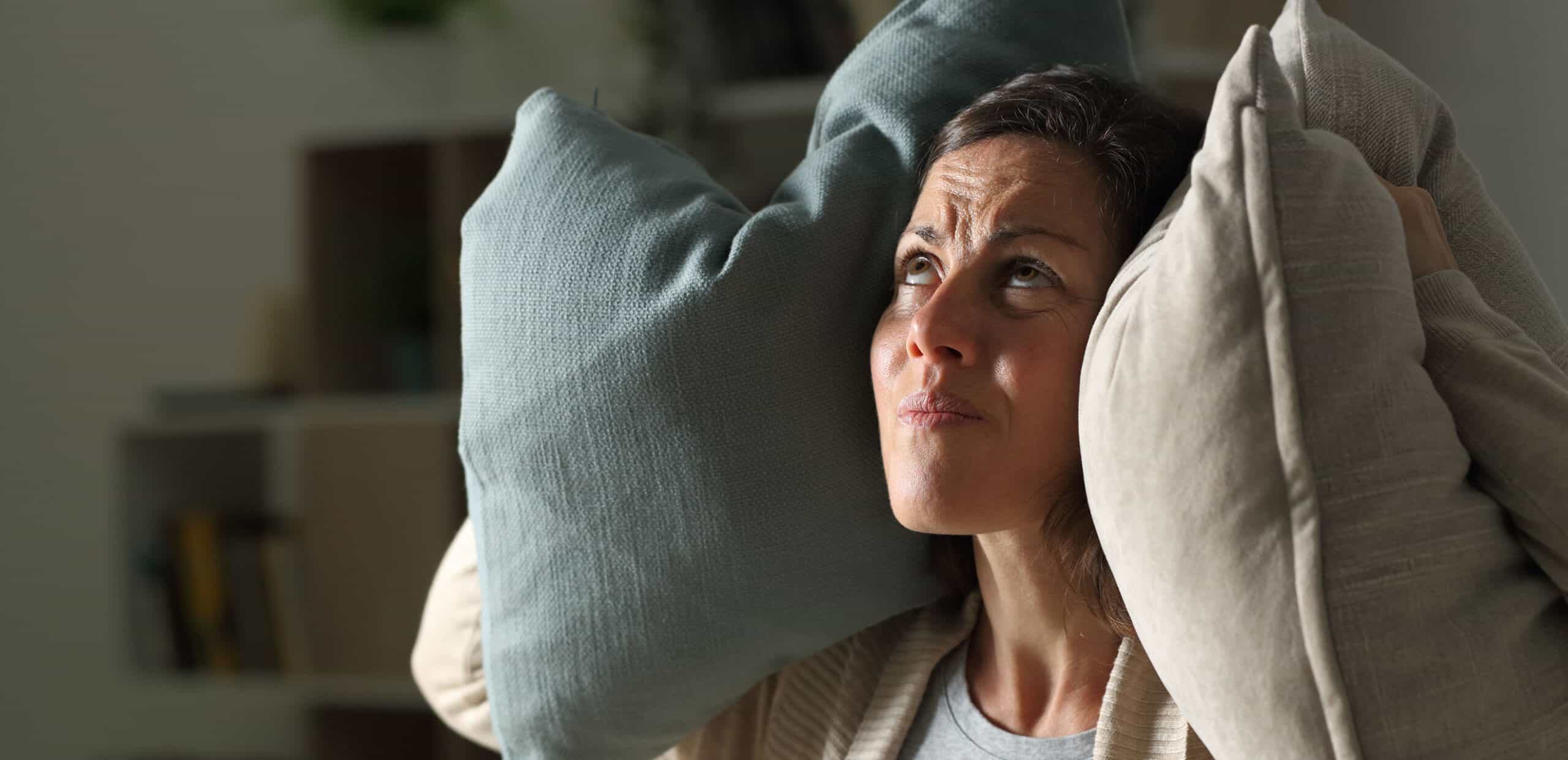 woman putting two pillows on either side of her ears to drown out noise.