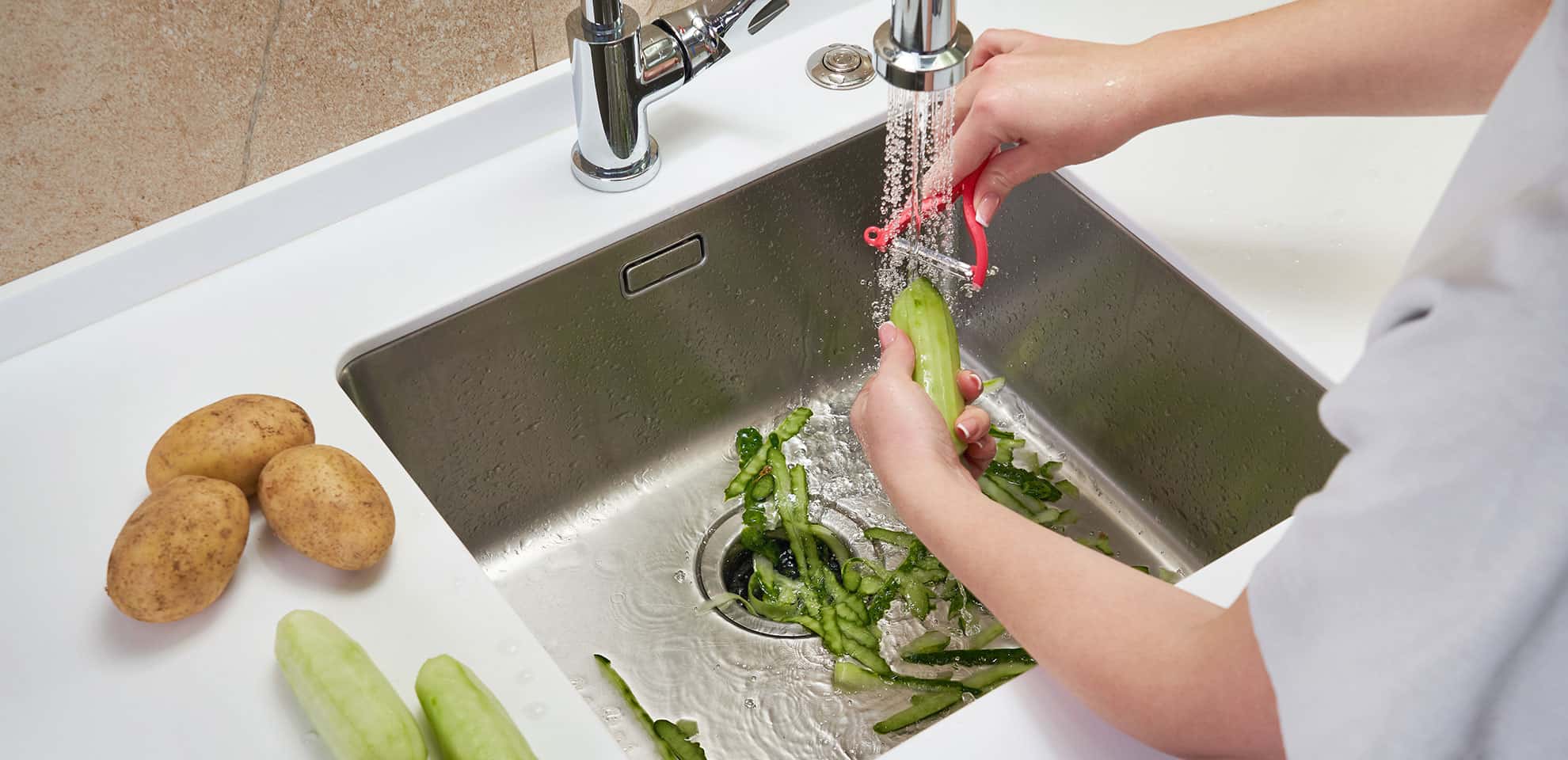 someone peeling a cucumber into a sink