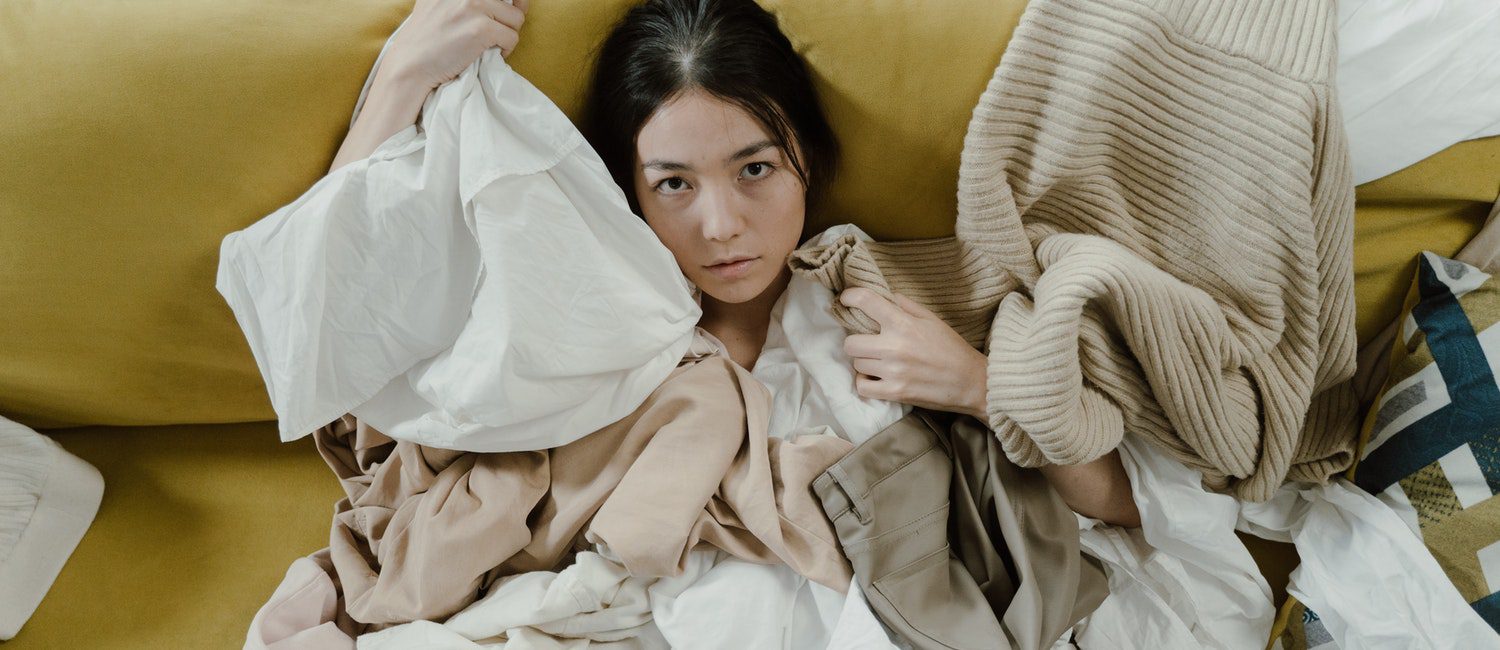 stressed woman on a couch surrounded by clothes wondering what to get rid of